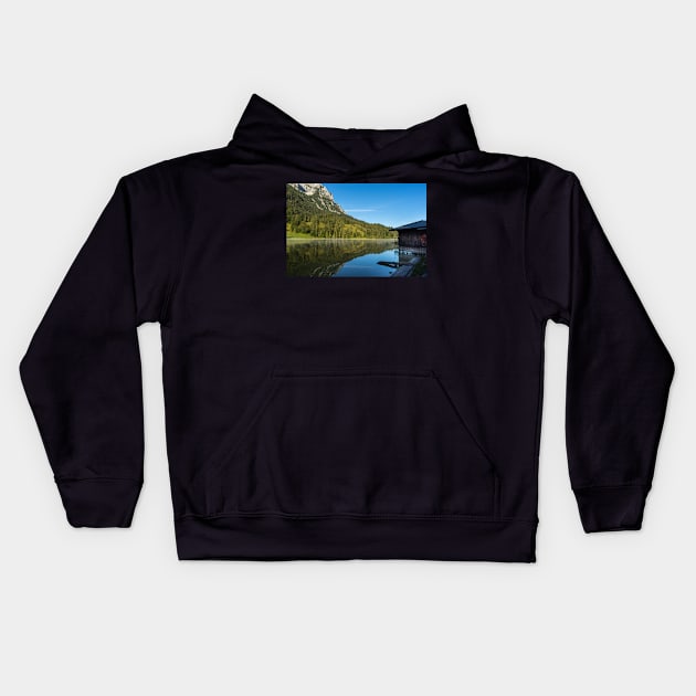 Lake water reflections with wooden boathouse wide angle. Amazing shot of a wooden house in the Ferchensee lake in Bavaria, Germany, in front of a mountain belonging to the Alps. Kids Hoodie by EviRadauscher